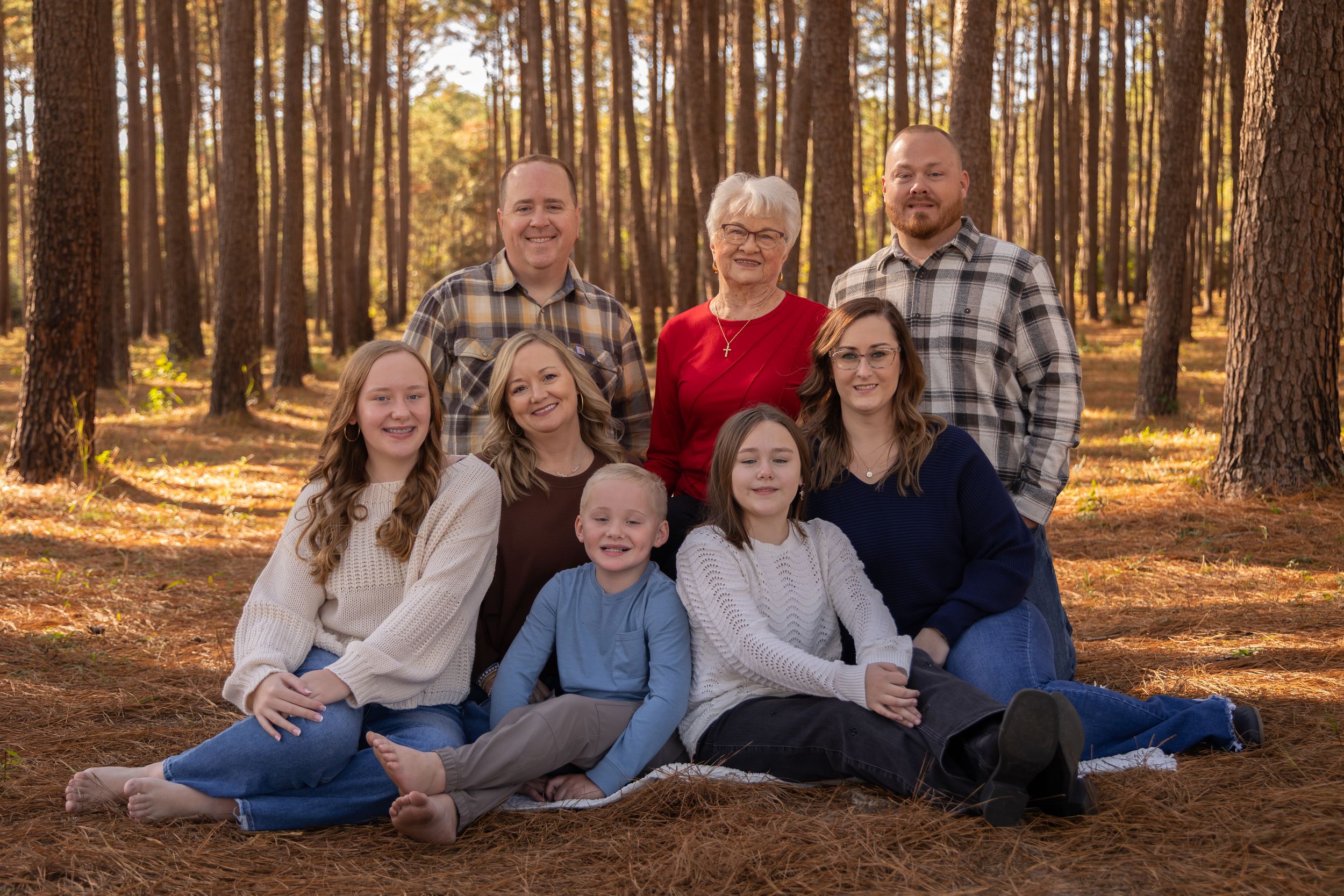 A group sits together on a fallen log in a sunlit autumn forest during a family photo session.