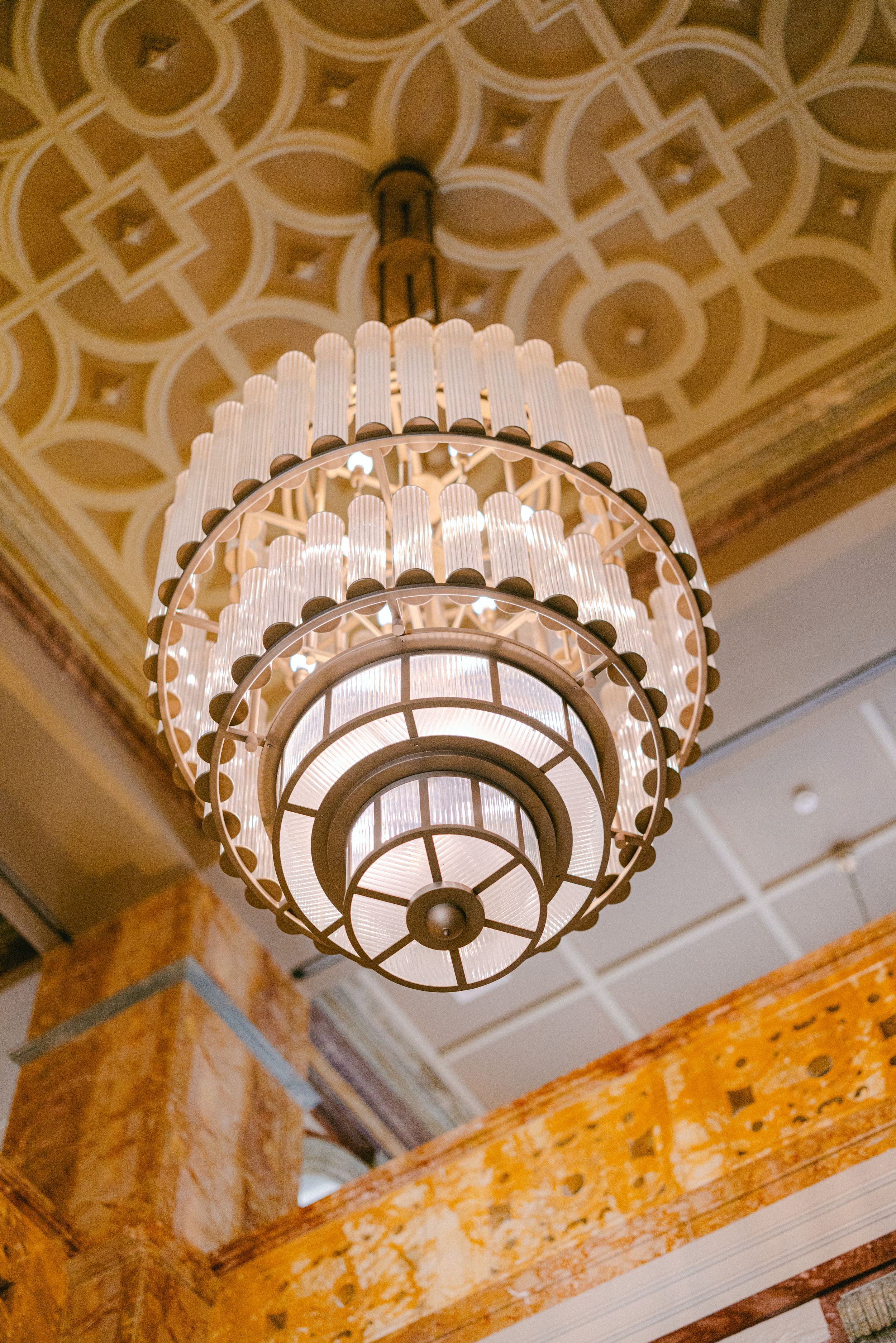 Elegant tiered crystal chandelier hanging from an ornately decorated ceiling with geometric patterns.