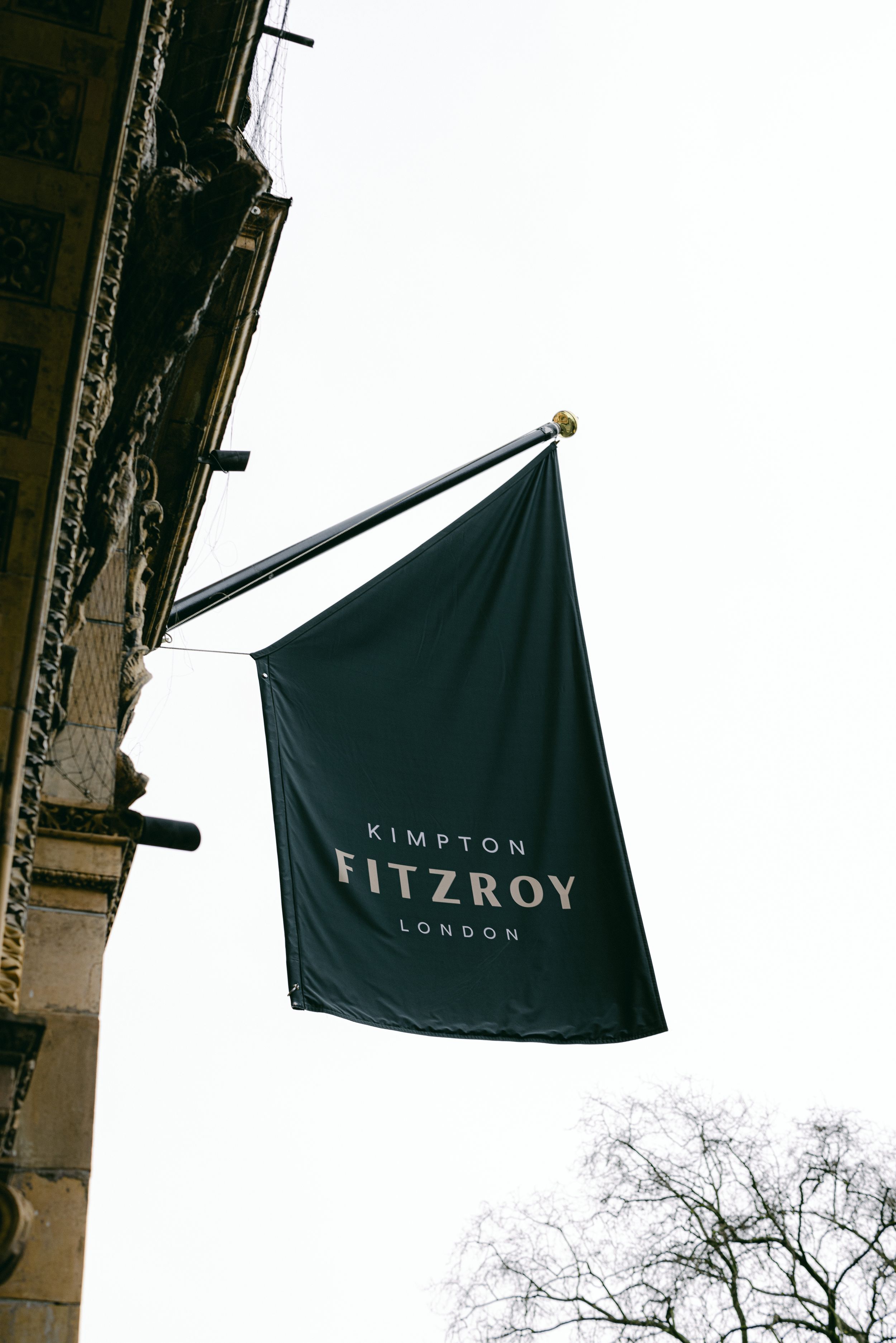 Black flag with Kimpton Fitzroy London branding mounted on building exterior.