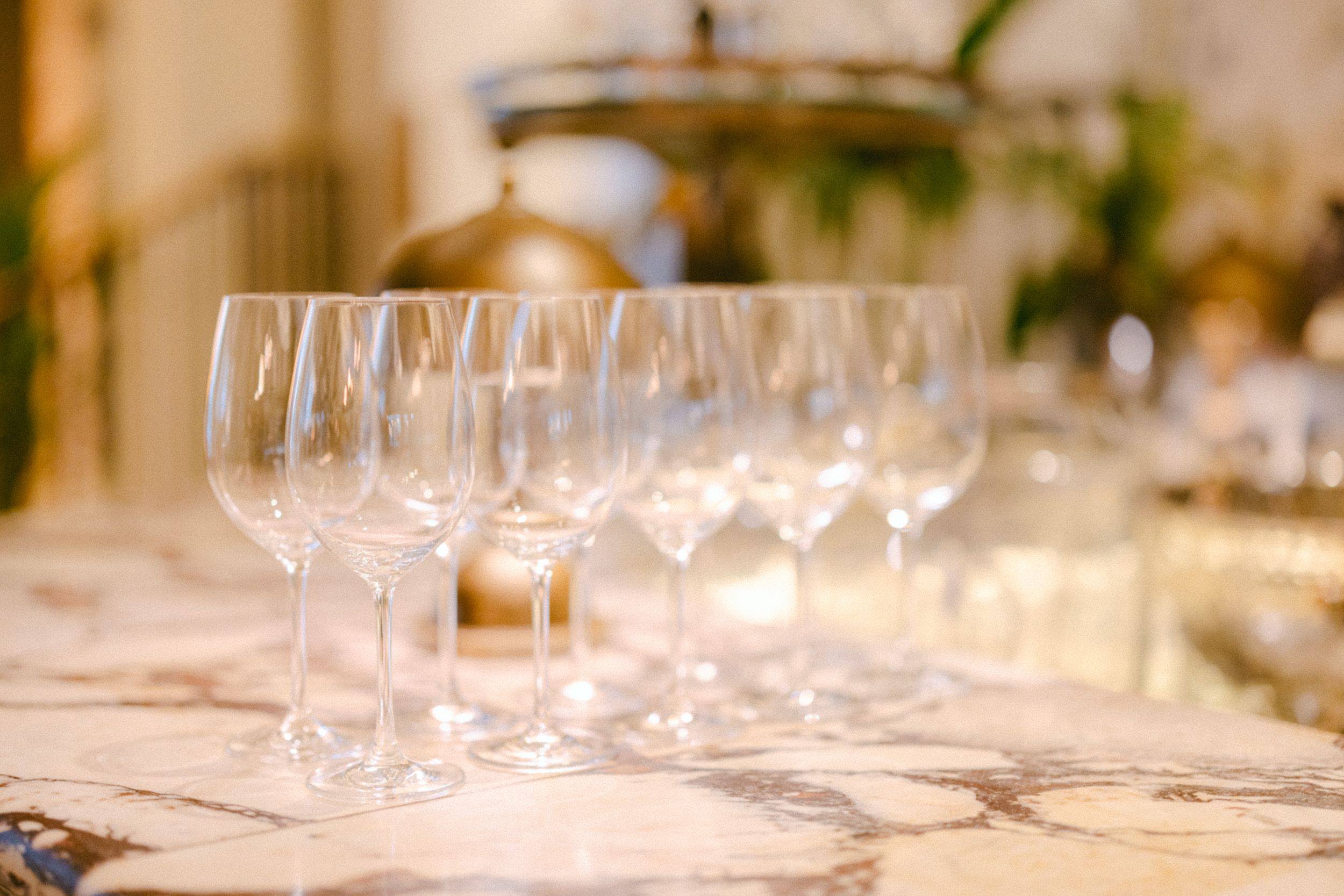 Row of empty wine glasses lined up on a white marble table setting.