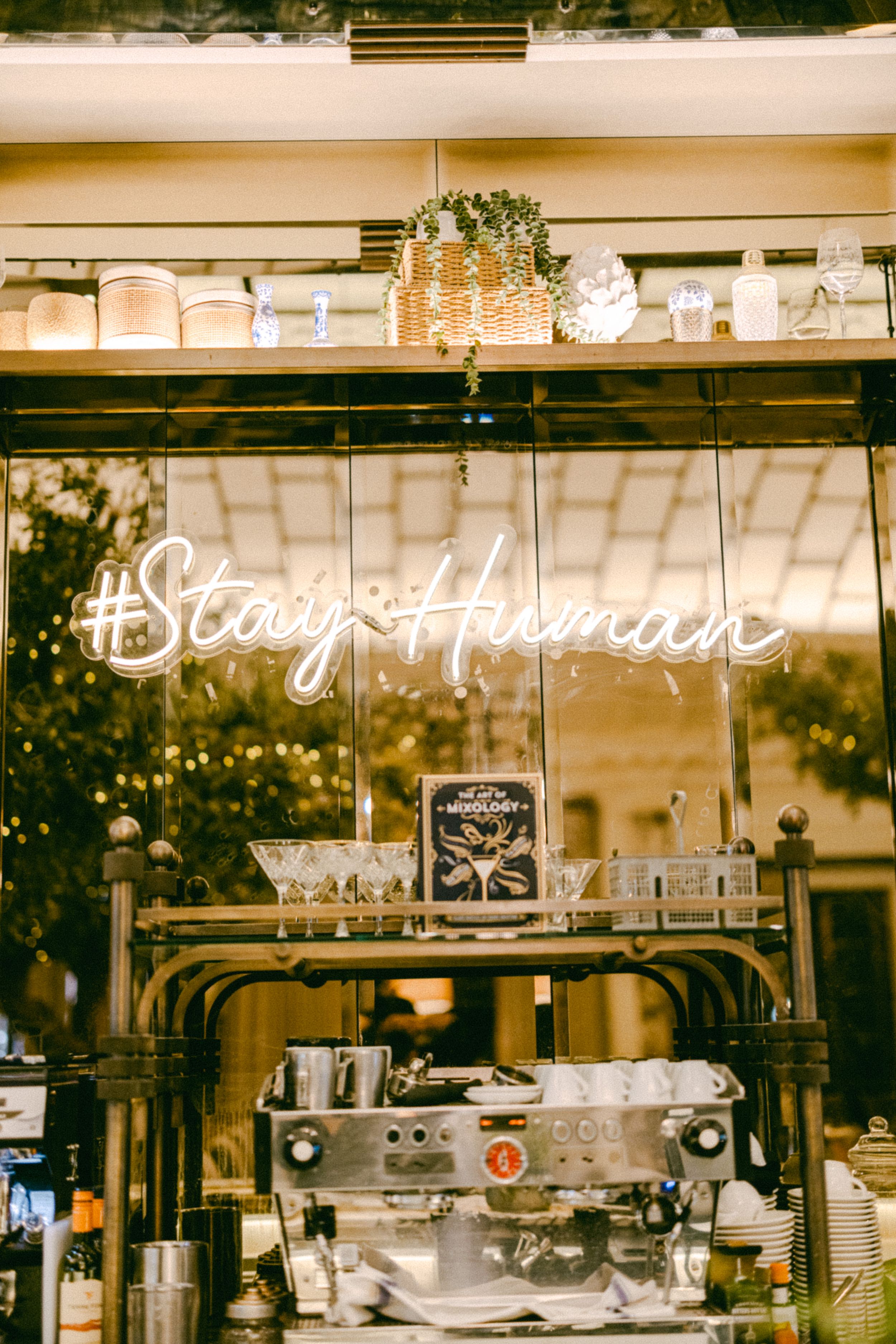 Coffee bar with neon 'Stay Human' sign and espresso machine display.