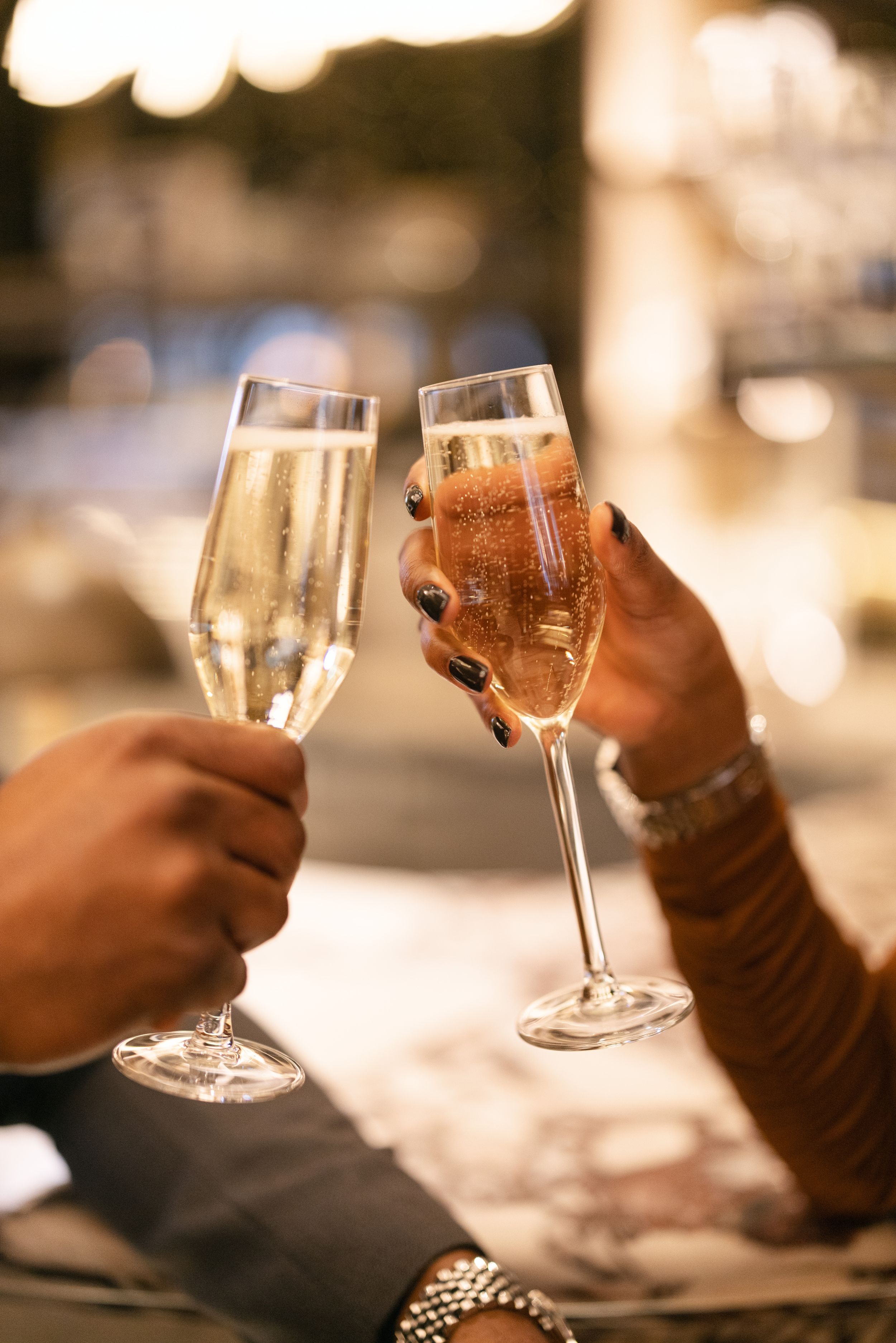 Two champagne flutes clinking in a toast against a warm, blurred background.