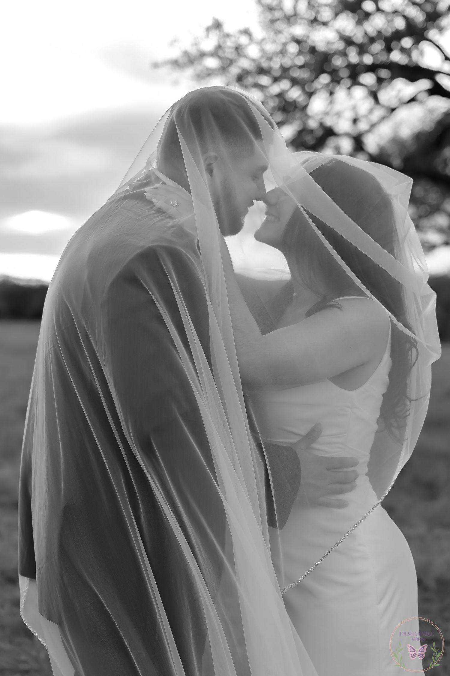 A romantic black and white photo of newlyweds sharing an intimate moment under their veils.