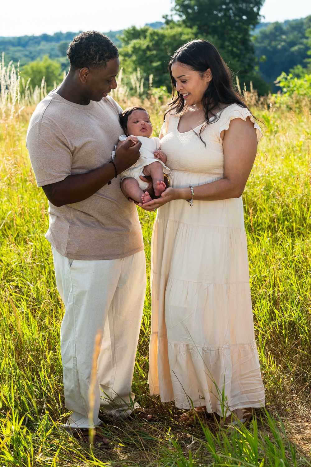 Family shares tender moment with newborn baby in sunny meadow at golden hour.
