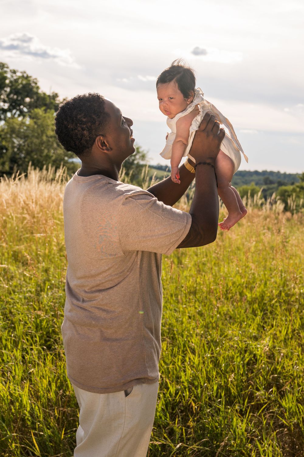 Parent lifts baby up in golden meadow during sunset photoshoot.