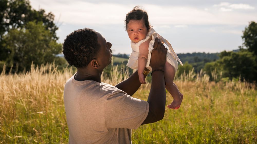Parent lifts infant during sunset photo session in meadow.