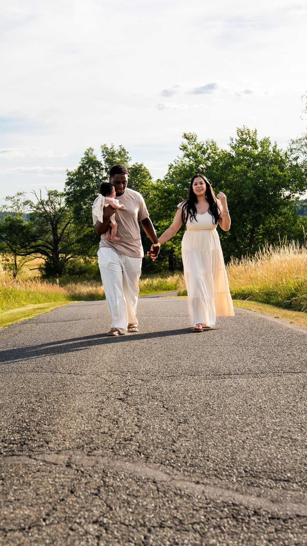 Couple walks hand in hand on rural road wearing coordinating white outfits.