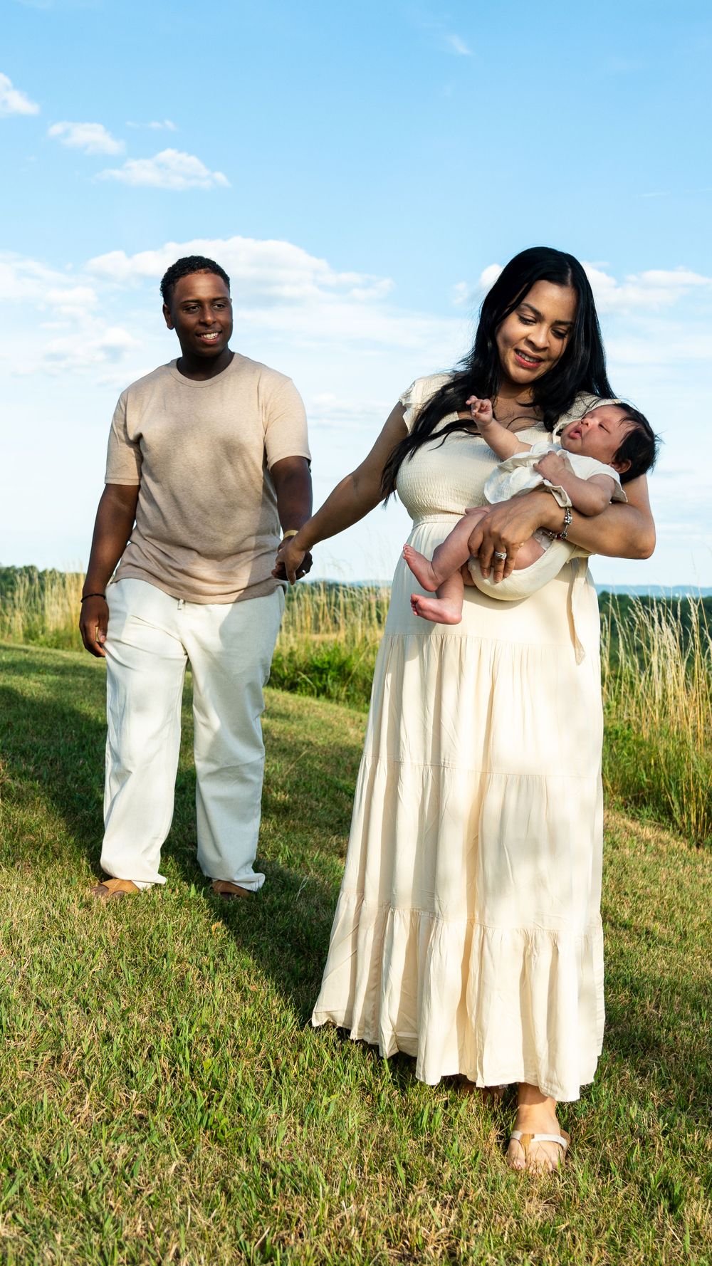 Family poses in grassy field with baby during outdoor portrait session.