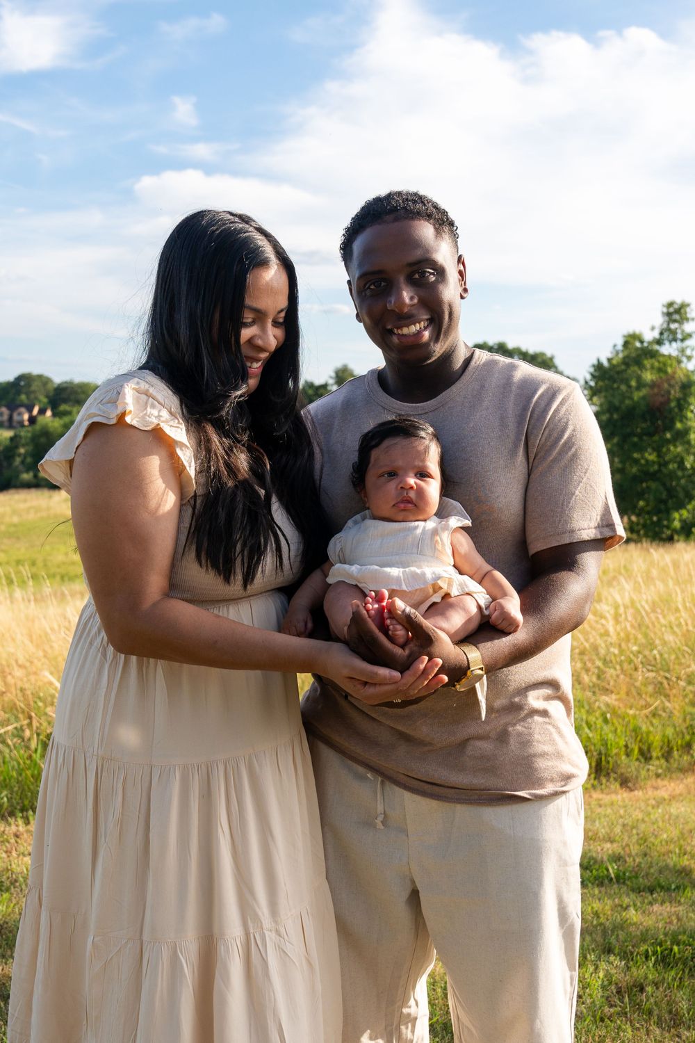 A family poses together outdoors in coordinated neutral outfits against a natural landscape.