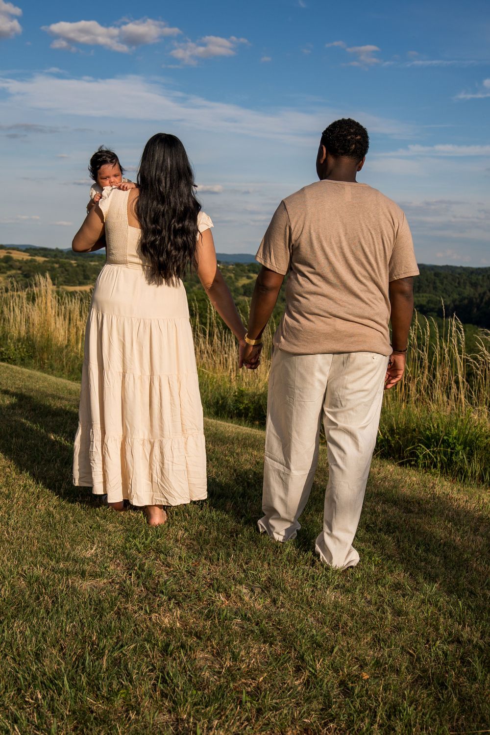 A family stands together overlooking a scenic hillside view on a sunny day.