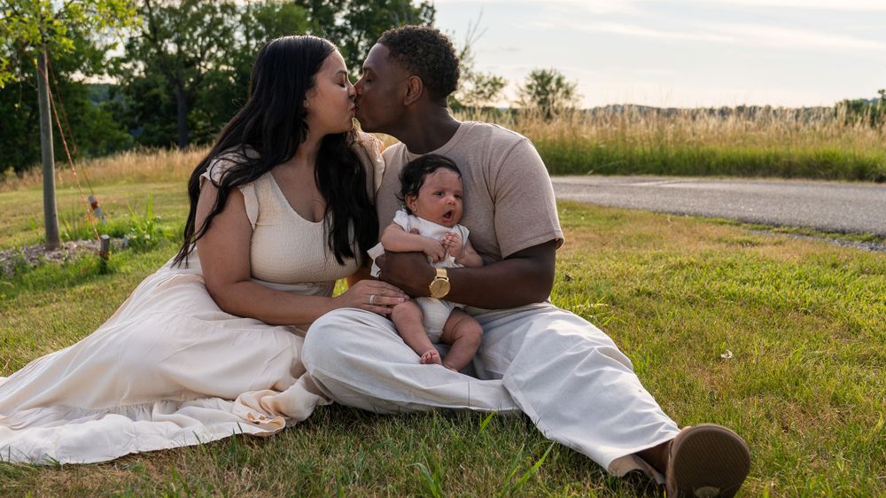 A family shares an intimate moment while sitting together on grass during a summer evening.