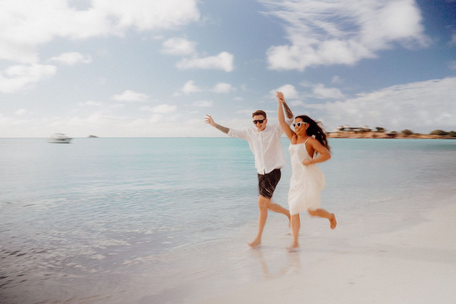 Carefree couple jumping with joy on white sandy beach.