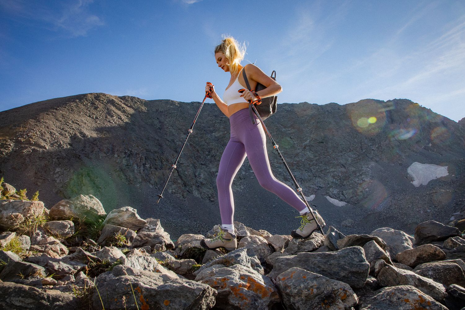 Person hiking across rocky terrain with trekking poles against mountain backdrop.