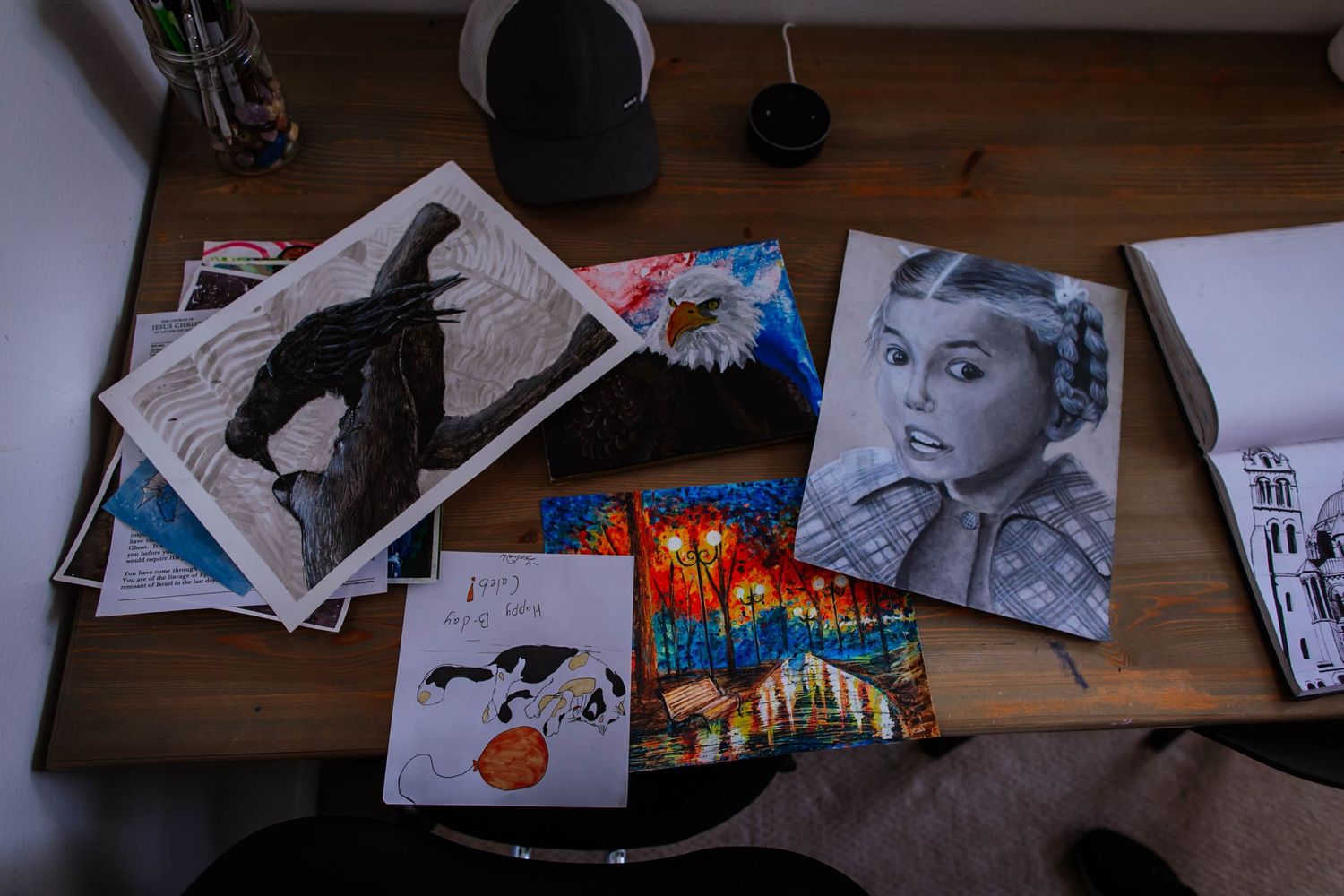Collection of photographs and artwork scattered across a wooden desk surface in moody lighting.