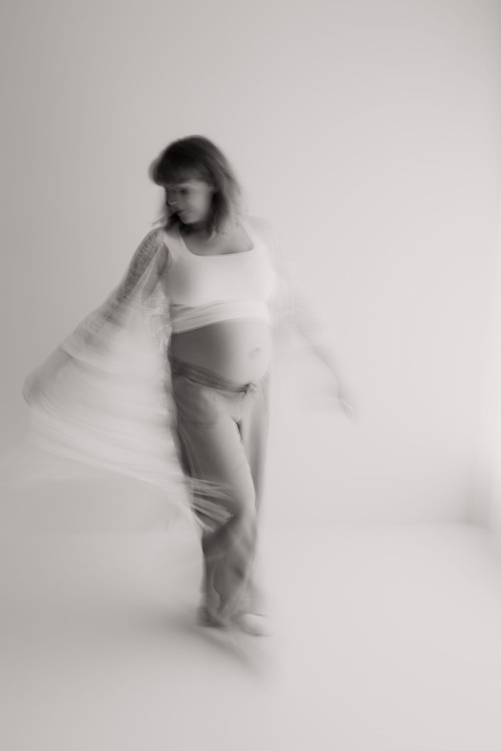 Abstract motion blur photograph shows a figure in white clothing creating ethereal movement against a light background.