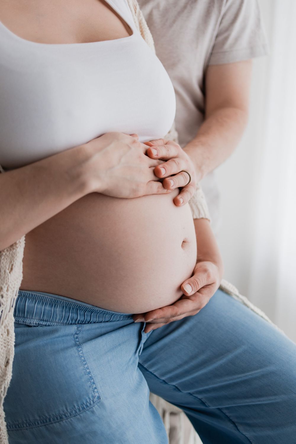 A series of photos showing a pregnant woman's growing belly while wearing jeans and a white top.