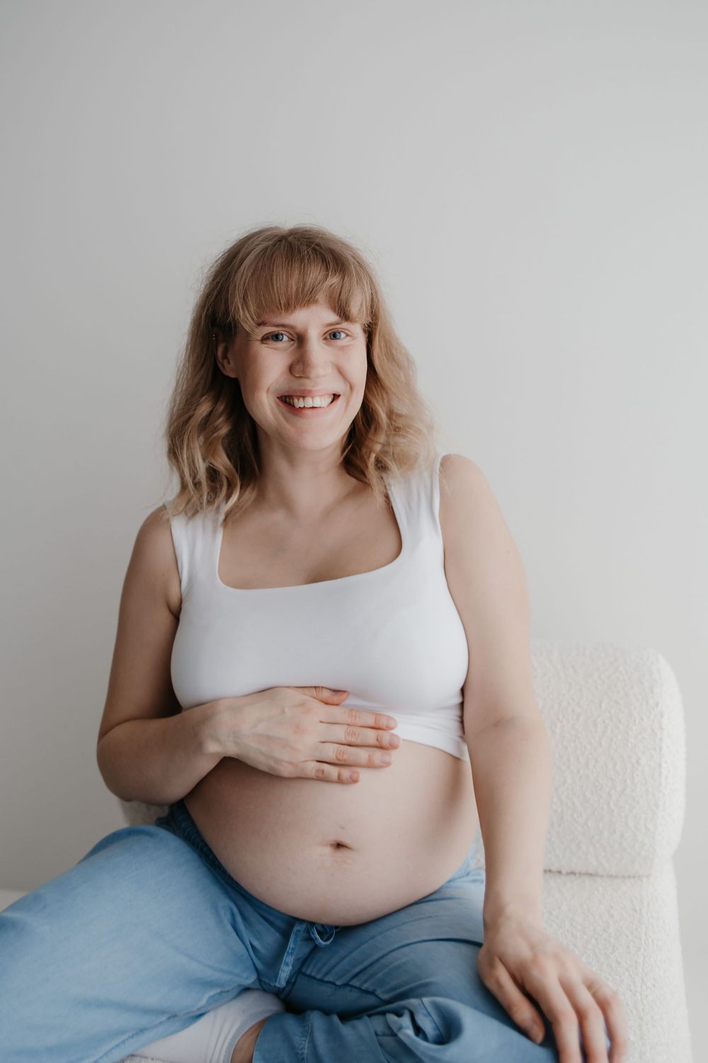 Four progressive photos show a person in white tank top and jeans sitting on white couch showing their belly.
