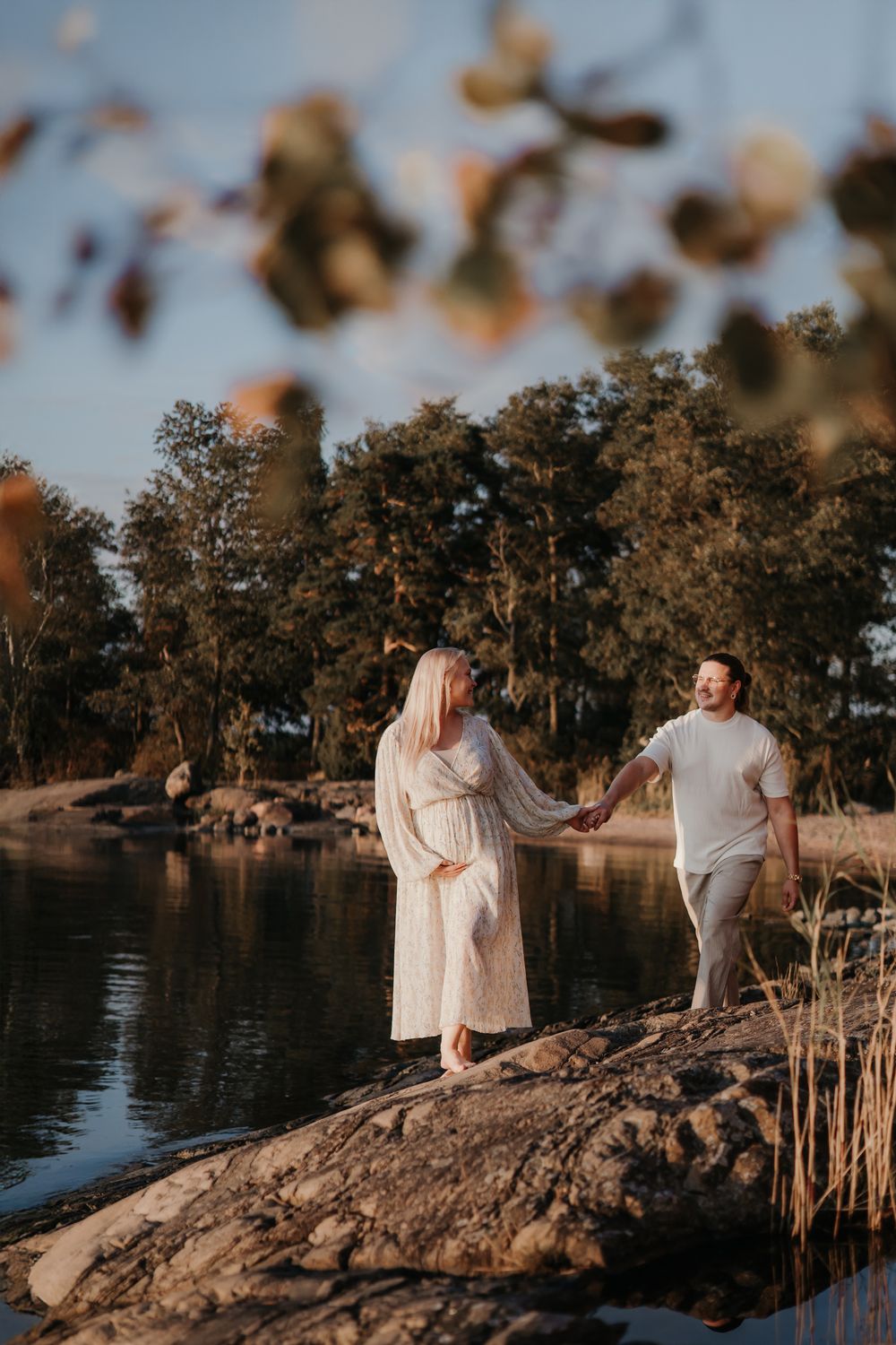 Couple in light clothing explores rocky waterfront during golden hour.