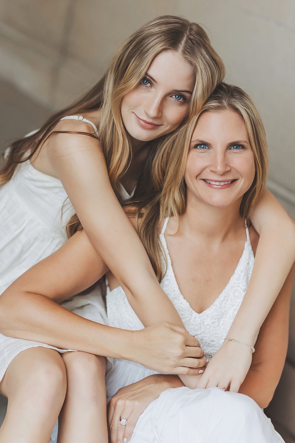 Two women in white dresses embrace while sharing a tender moment.