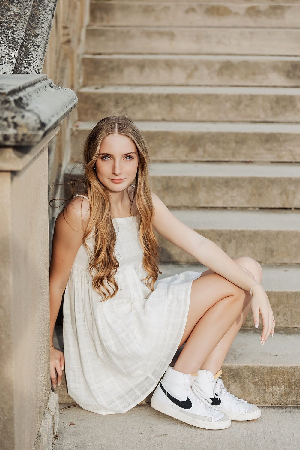 Fashion portrait on stone steps featuring white summer dress and Nike sneakers.