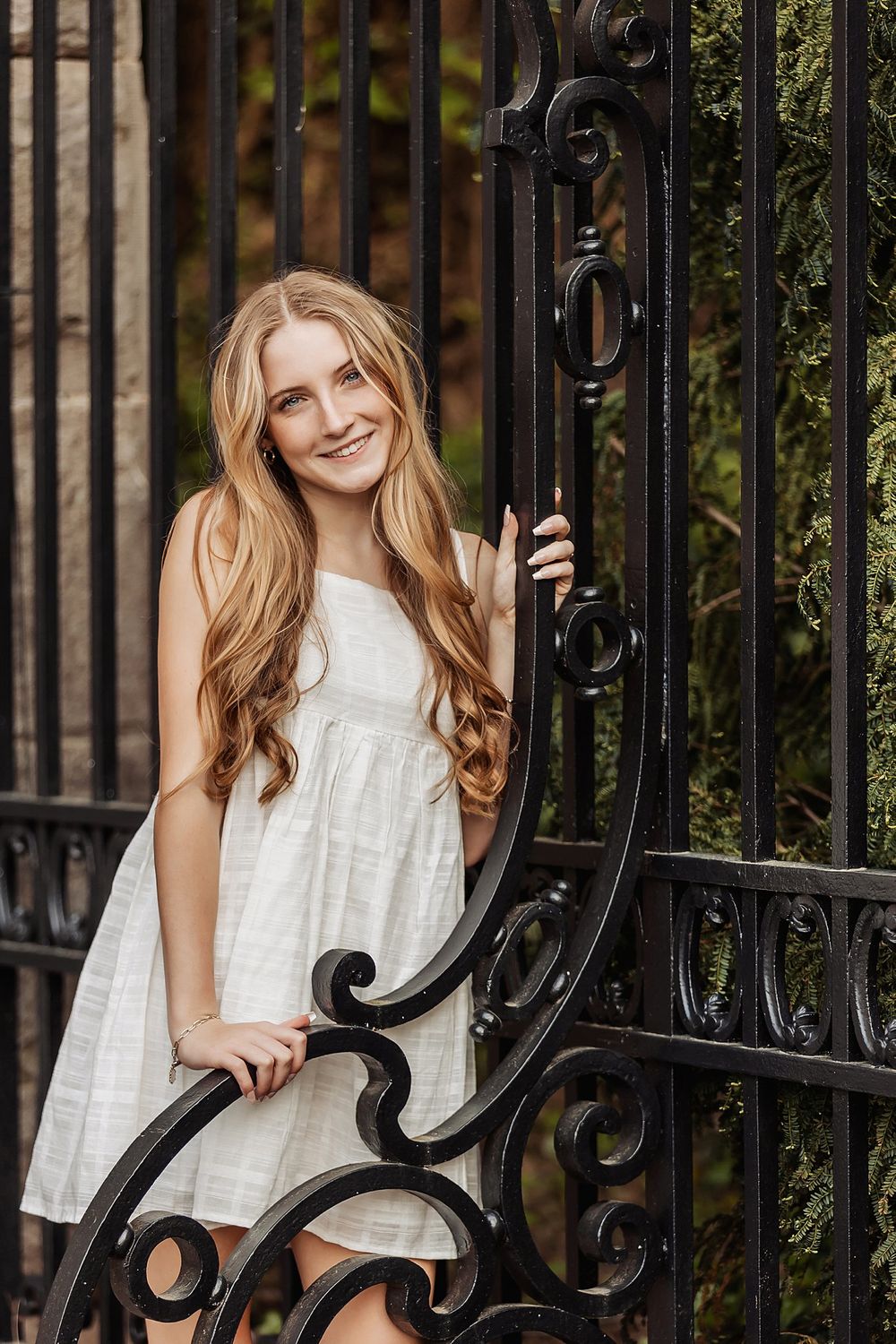 White dress and ornate iron gate create an elegant portrait setting with natural lighting.