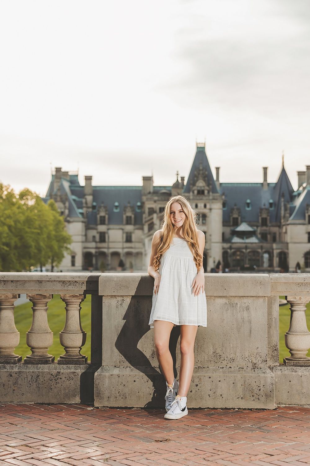 White summer dress contrasts against historic castle architecture and stone balustrade.