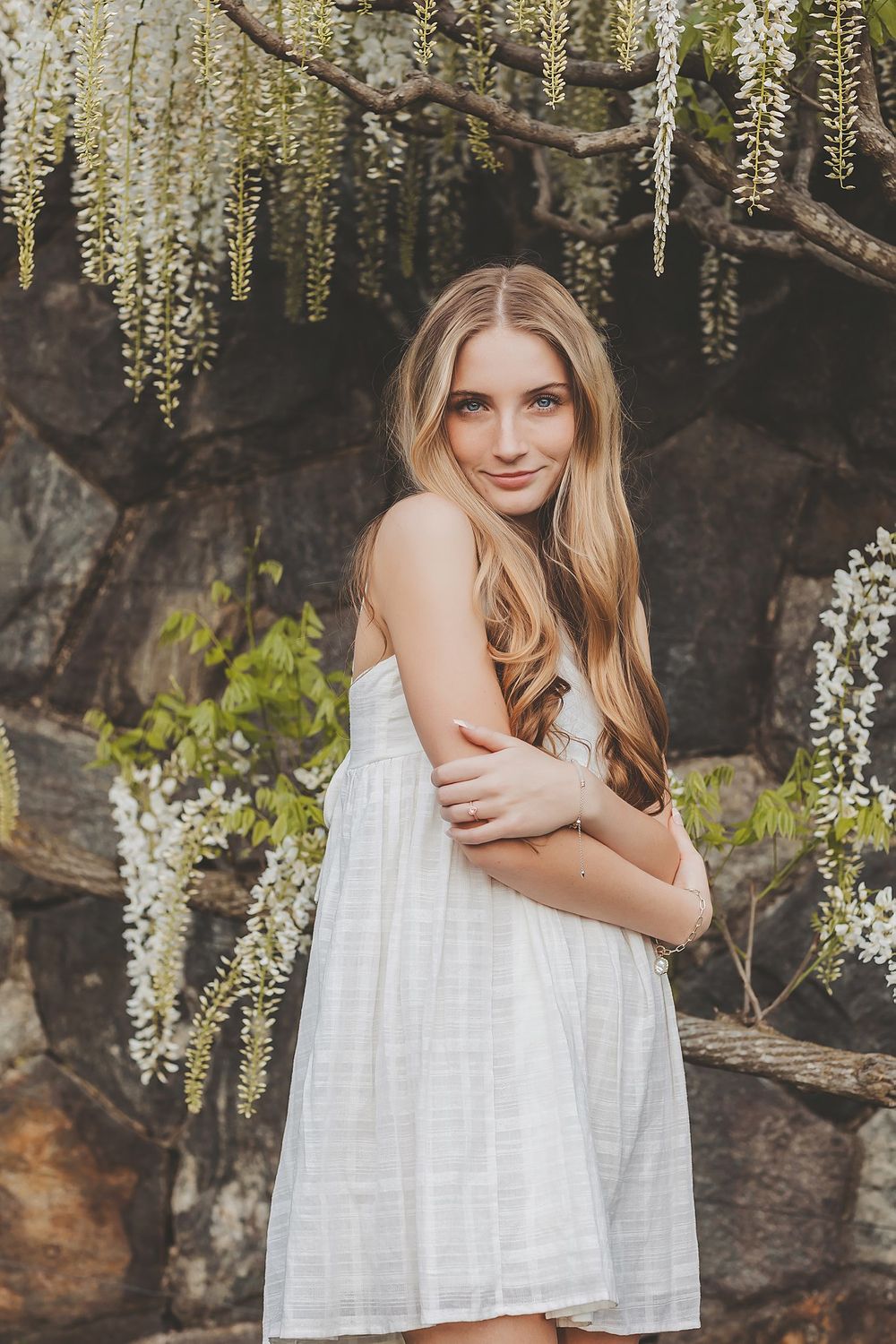 Ethereal portrait under hanging wisteria flowers with natural stone backdrop.