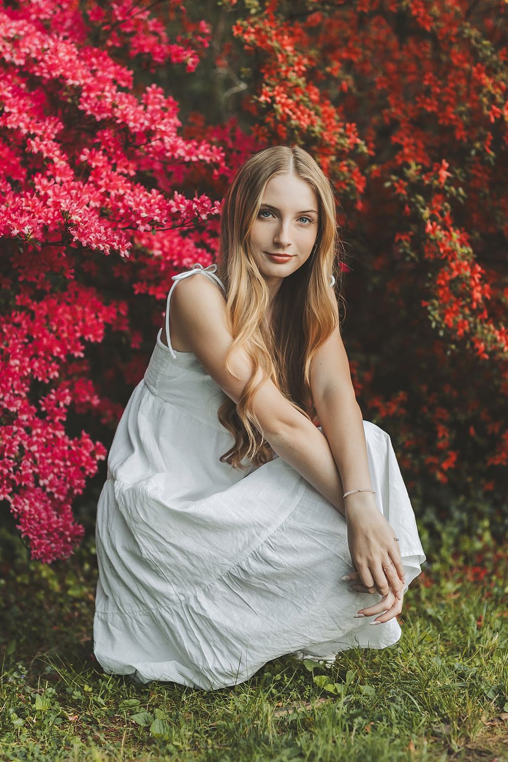 White sundress contrasts beautifully with vibrant pink azalea flowers in outdoor portrait.