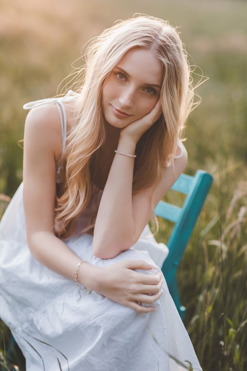 Dreamy summer portrait in white dress amid tall grass field.