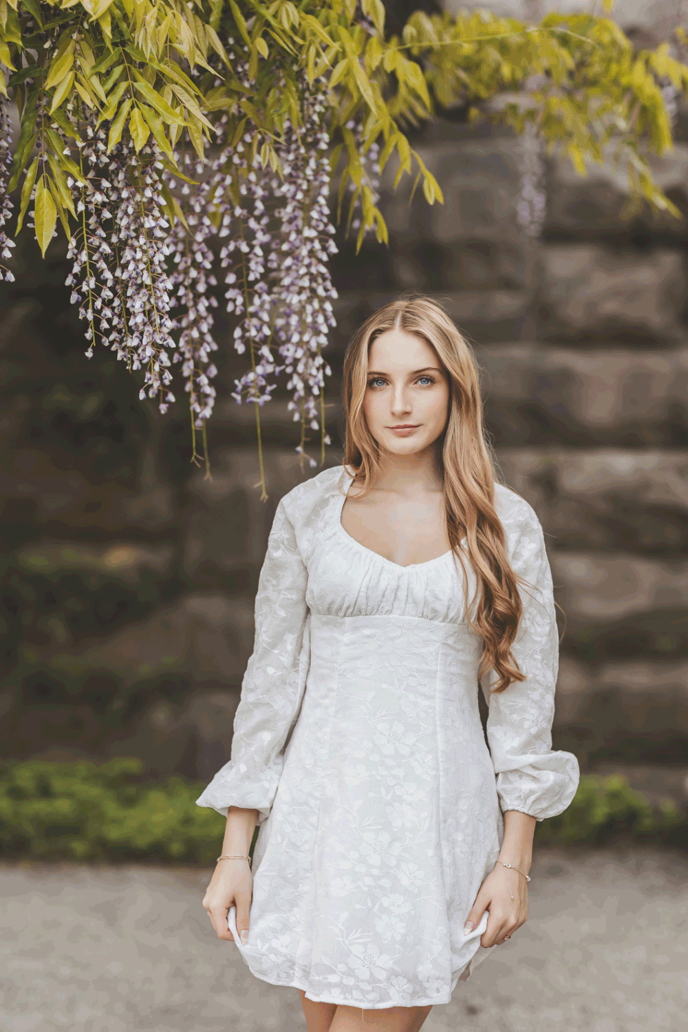A white lace dress with puff sleeves photographed under blooming wisteria flowers.