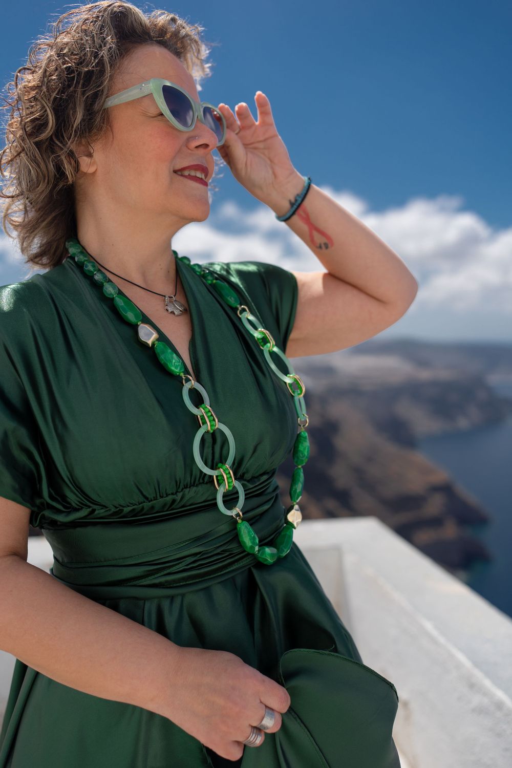 Summer fashion with green dress and matching accessories against Mediterranean backdrop.