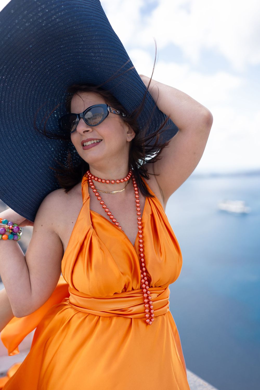 Navy sun hat and orange dress against Mediterranean Sea backdrop.