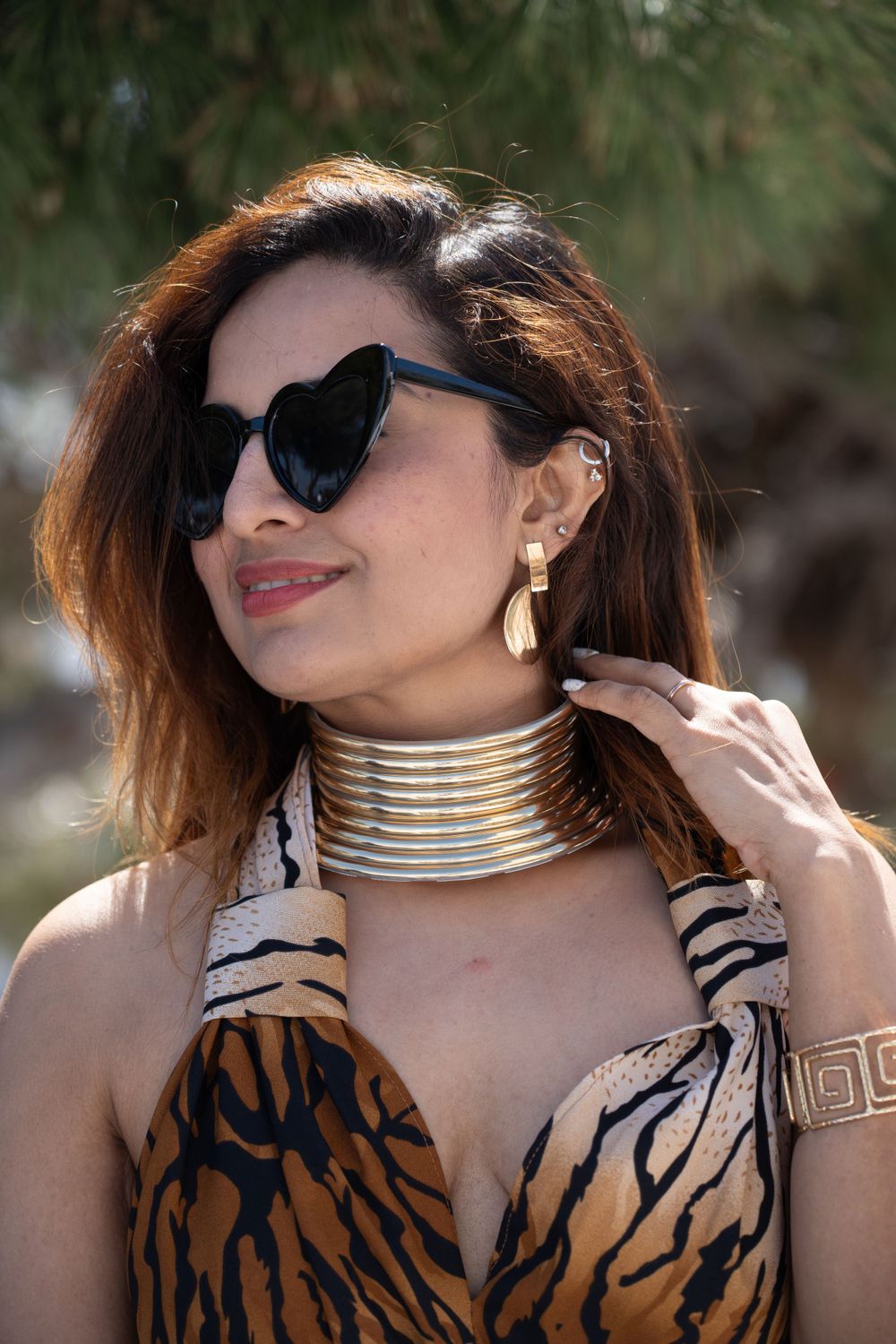 Animal print dress with gold choker necklace and heart-shaped sunglasses in natural lighting.