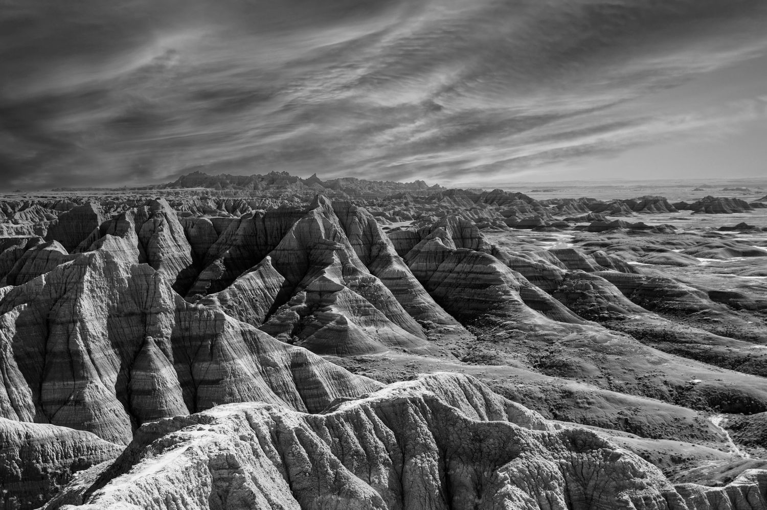 Black and white landscape of eroded rock formations in the Badlands under dramatic cloudy sky.