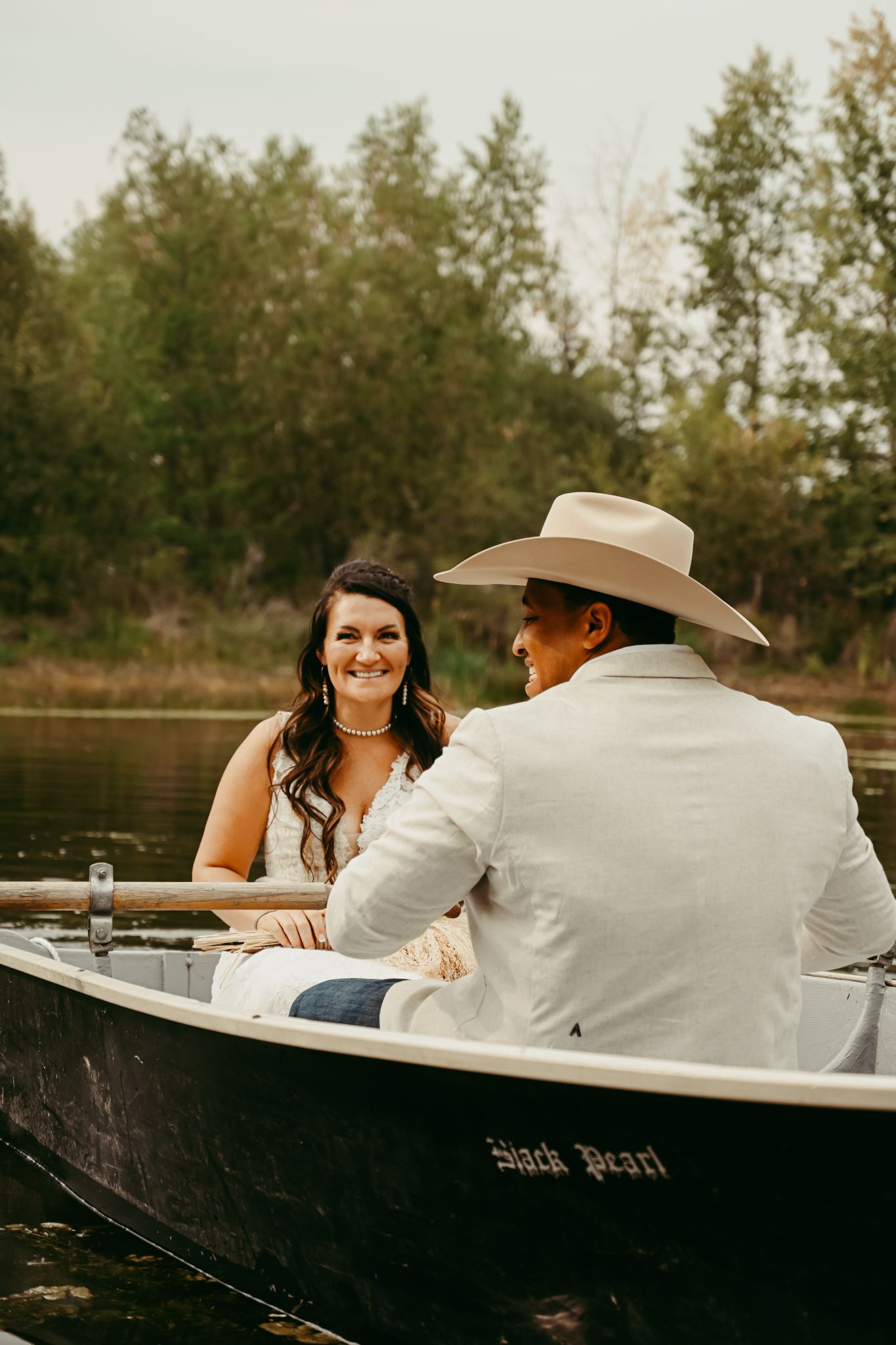 A couple shares a romantic moment in a rowboat on a peaceful lake surrounded by trees.