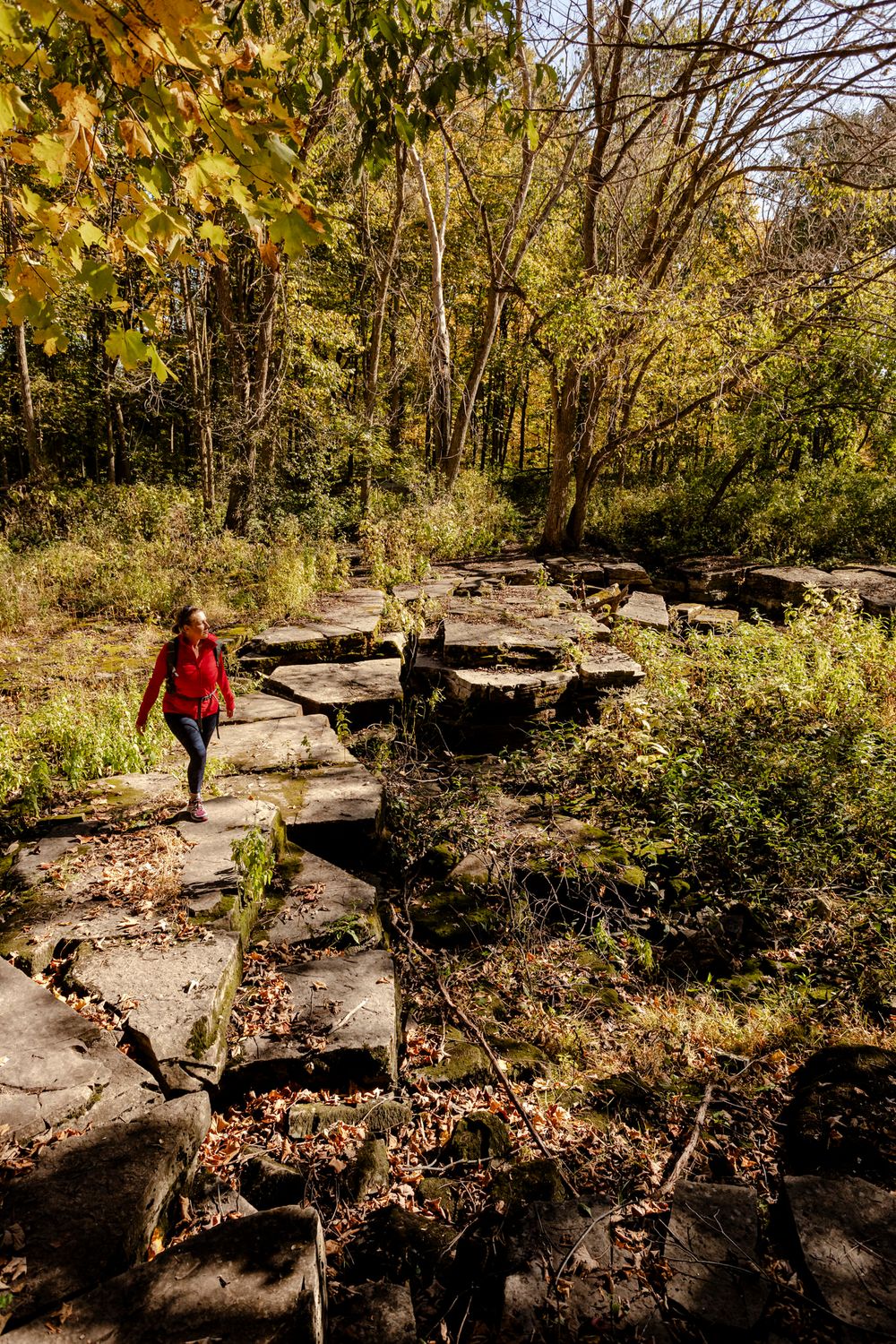 Alison of Lumenali Photography hikes across a dry, limestone river in rural wooded area of Kingston, Ontario, Canada.