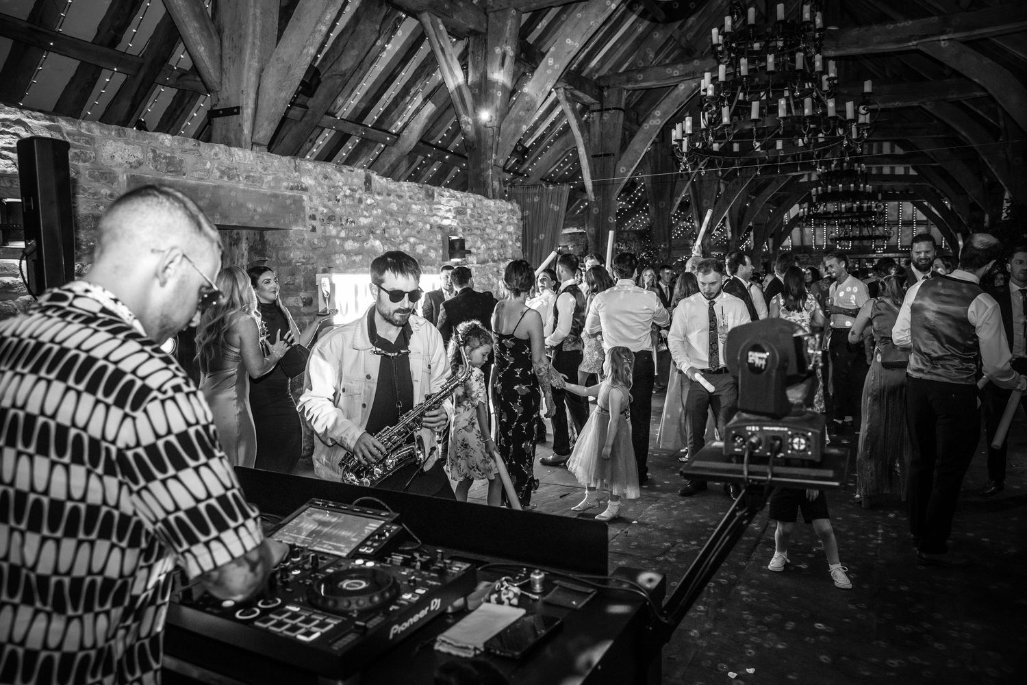 Black and white photo of DJ performing at lively rustic barn wedding reception dance floor.