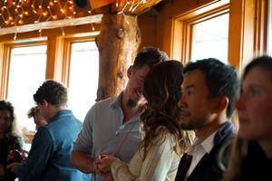 People gather in a rustic wood-paneled room decorated with string lights.