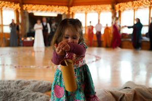 Wedding guests dancing and celebrating on a wooden dance floor under warm string lights.