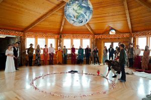 Wedding ceremony guests gather in a rustic wooden octagonal room with string lights and decorative circular floor layout.
