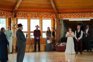 Wedding ceremony in a rustic wooden room with large windows and string light decorations.