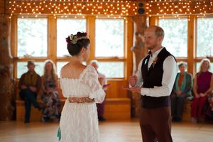 Wedding ceremony inside a wooden hall decorated with string lights.