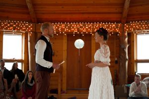Wedding ceremony taking place in a rustic wood-paneled room with string lights.