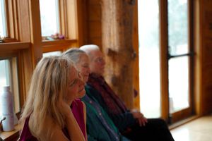 Interior of a wooden lodge with large windows and warm lighting showing guests gathered for an event.