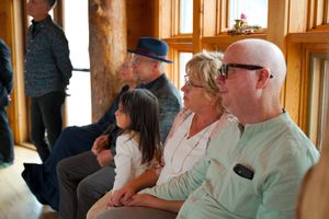 Wedding guests seated along windows in a wood-paneled reception venue.