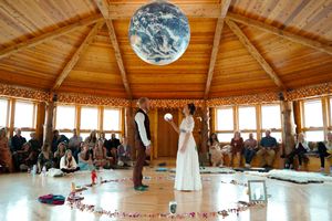A wedding ceremony space with wooden architecture and large windows features a prominent Earth globe overhead.