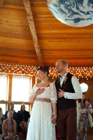 Guests dancing under globe lanterns at rustic venue with wood beam ceiling and string lights.