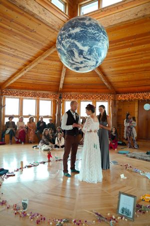Rustic wedding ceremony under a large Earth globe pendant light in wooden octagonal room with string lights.