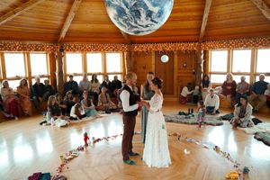 Panoramic view of a rustic wooden wedding venue with guests seated in circular formation during a ceremony.