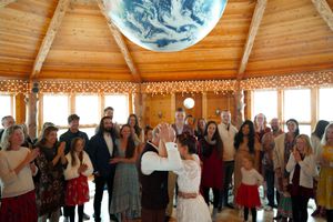 Wedding guests celebrate with dancing under a large Earth globe in an octagonal wooden venue.